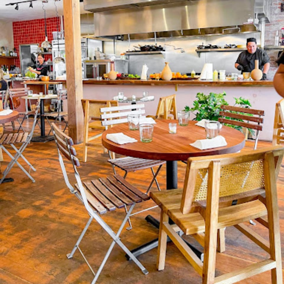 LOLA's open kitchen with chefs preparing Mexican food, and dining tables set for guests.
