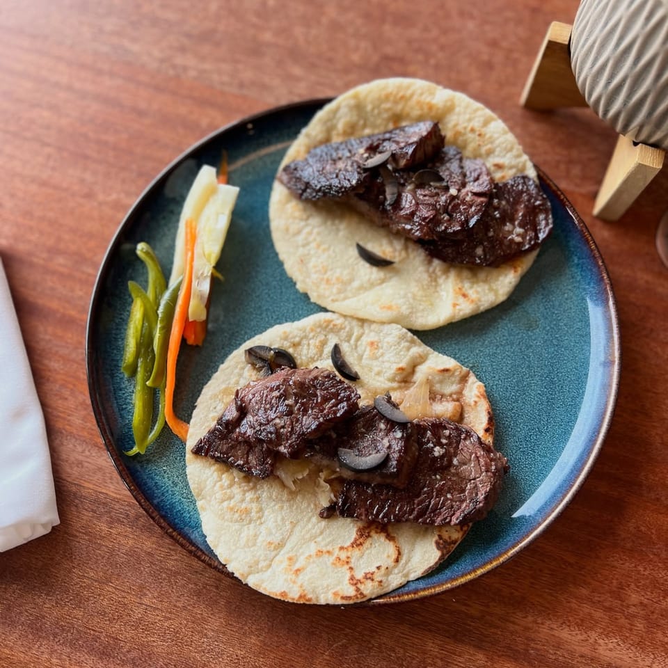 Two LOLA Mexican tacos with dark meat, black olives, and pickled vegetables on a blue plate.