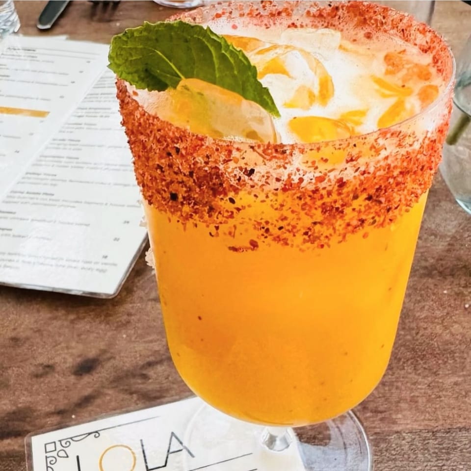 A vibrant yellow mango margarita with a chili-lime rim and mint garnish on a wooden table.