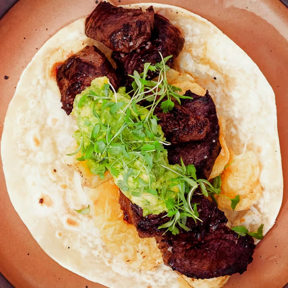LOLA's carne asada taco with guacamole, microgreens, and potato chips on a tortilla.