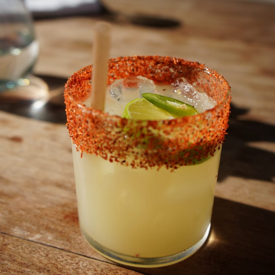 A spicy margarita with a chili-lime rim, lime, and jalapeño slices on a wooden table.