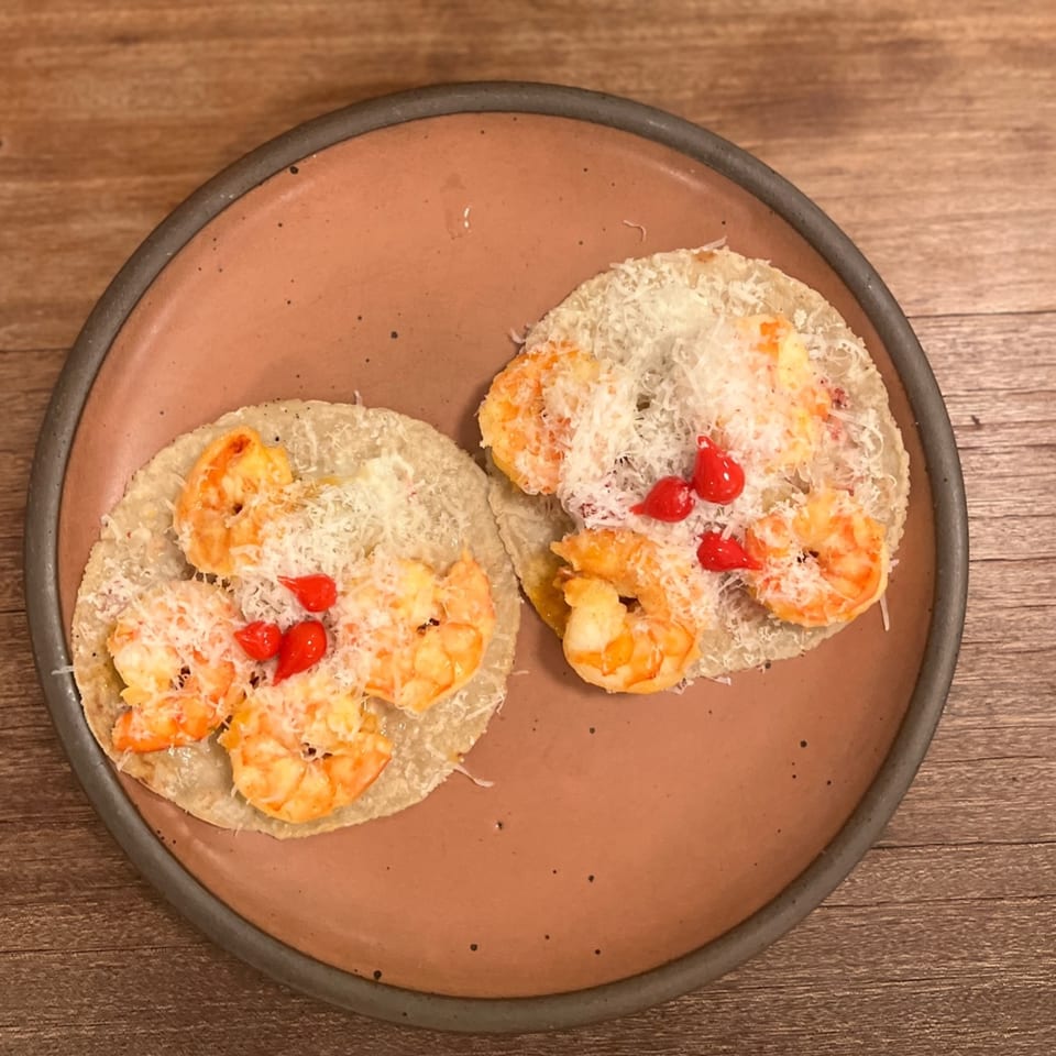 Two shrimp tacos with shredded cheese and red peppers on a rustic plate.