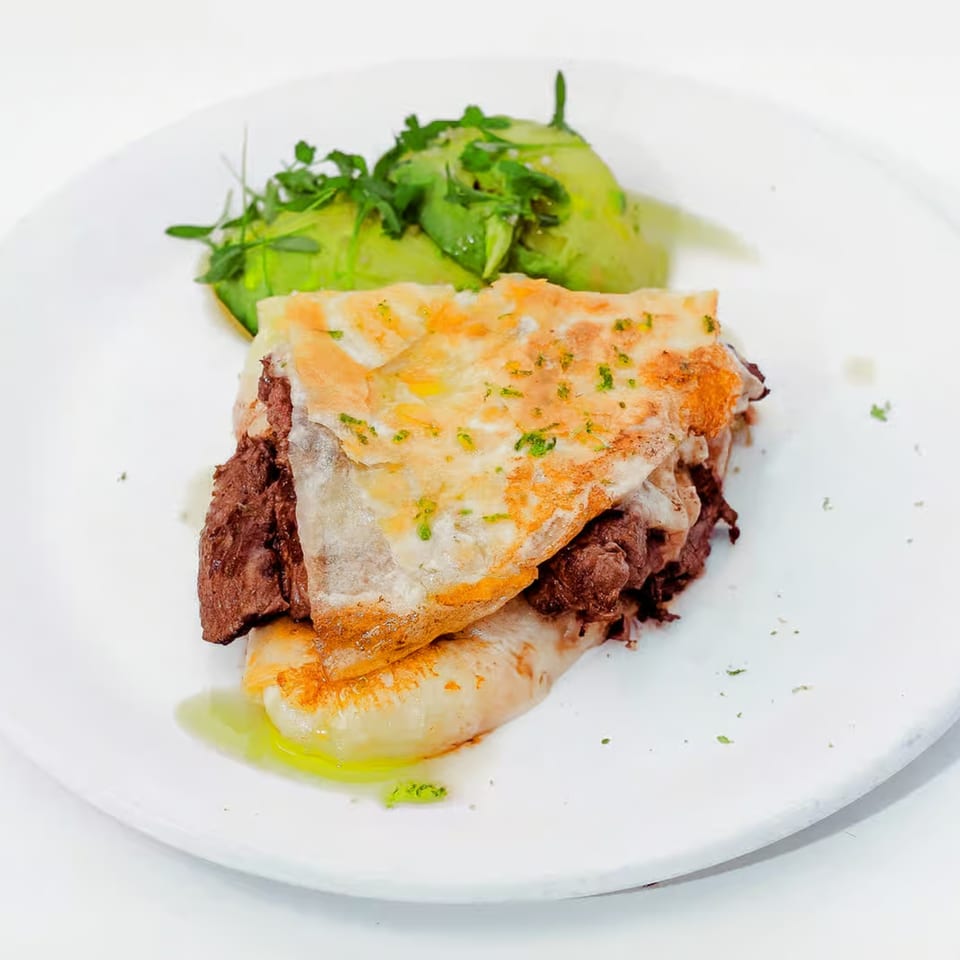 A Mexican dish with a golden-brown tortilla filled with dark meat, served with avocado slices.