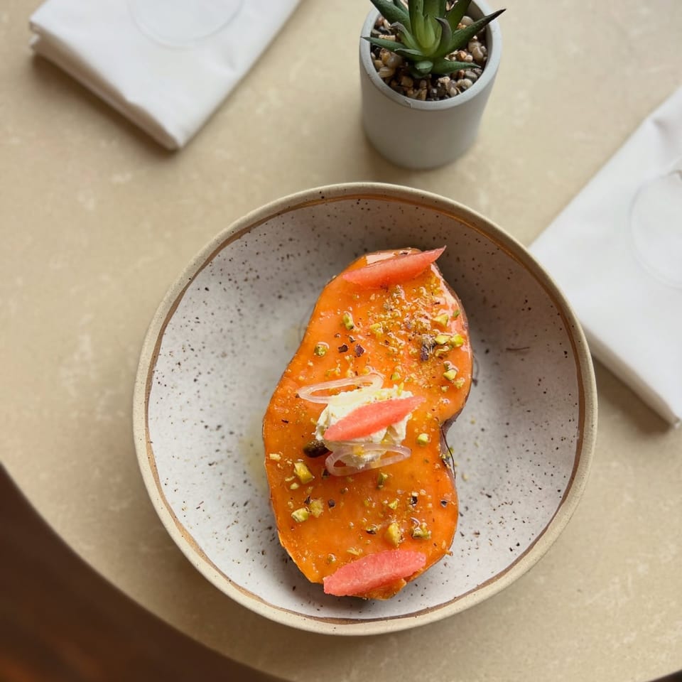 Overhead view of a vibrant orange Mexican dish with pistachios, cream, and grapefruit slices in a speckled bowl.