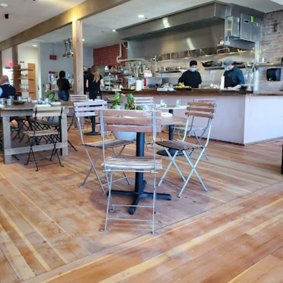 LOLA restaurant interior with wooden floors, tables, chairs, and kitchen staff working in the background.