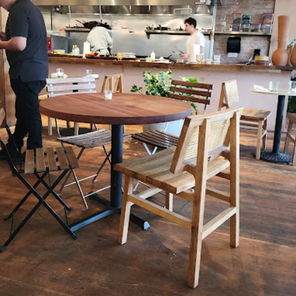 LOLA restaurant interior with wooden tables and chairs, and chefs working in the open kitchen.